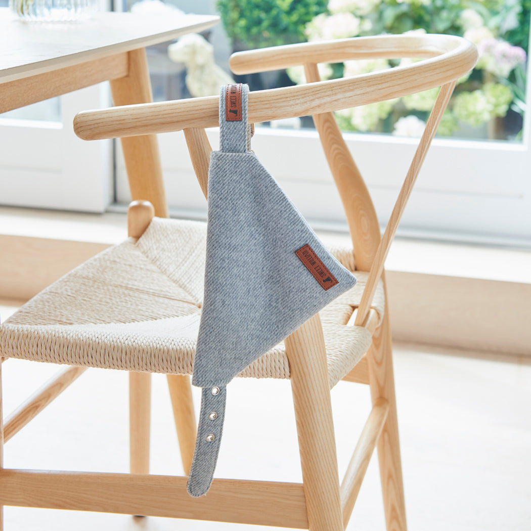 Grey tweed dog bandana threaded onto its matching collar, displayed on a wooden chair with the Sweet William label showing