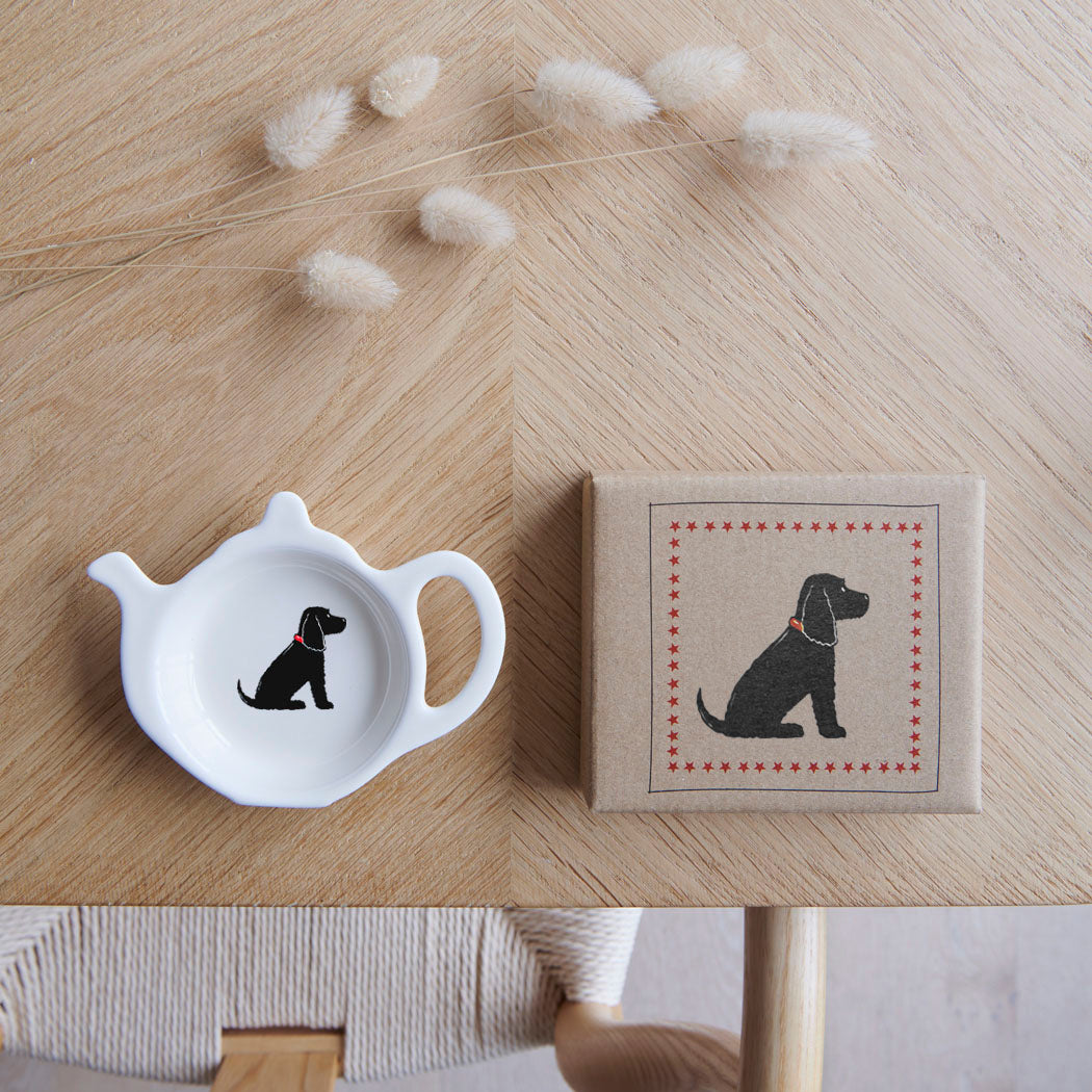 White teapot-shaped Black Cocker Spaniel teabag dish beside its kraft gift box, both featuring a black Spaniel illustration with a red collar