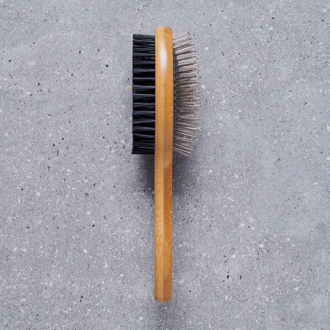 Bamboo double sided dog brush on grey stone surface showing both sides — bristle side and pin side, dog grooming brush by Sweet William Designs