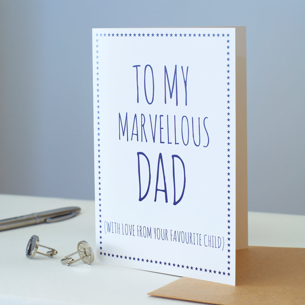 White Dad card standing beside a kraft envelope, silver cufflinks and a pen, with blue lettering reading “To My Marvellous Dad” and “With love from your favourite child”.