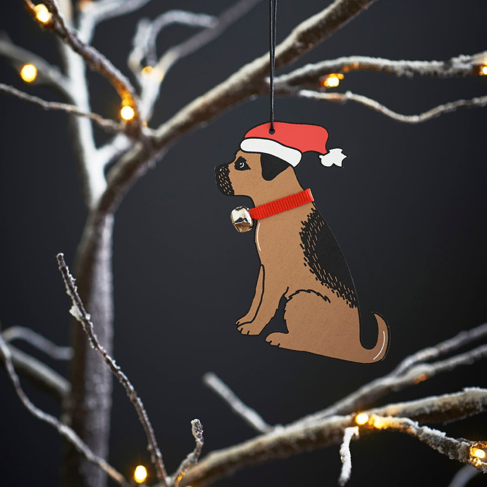 Border Terrier Christmas tree decoration hanging on lit winter tree — wooden dog decoration with Father Christmas hat and jingle bell collar by Sweet William Designs