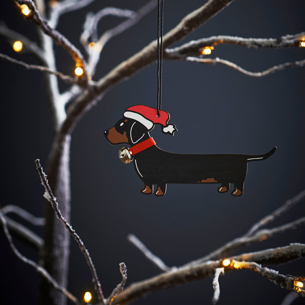 Dachshund Christmas tree decoration hanging on lit winter tree — wooden dog decoration with Father Christmas hat and jingle bell collar by Sweet William Designs