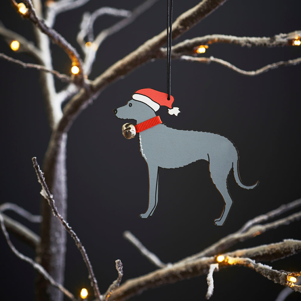 Lurcher Christmas tree decoration hanging on lit winter tree — wooden dog decoration with Father Christmas hat and jingle bell collar by Sweet William Designs