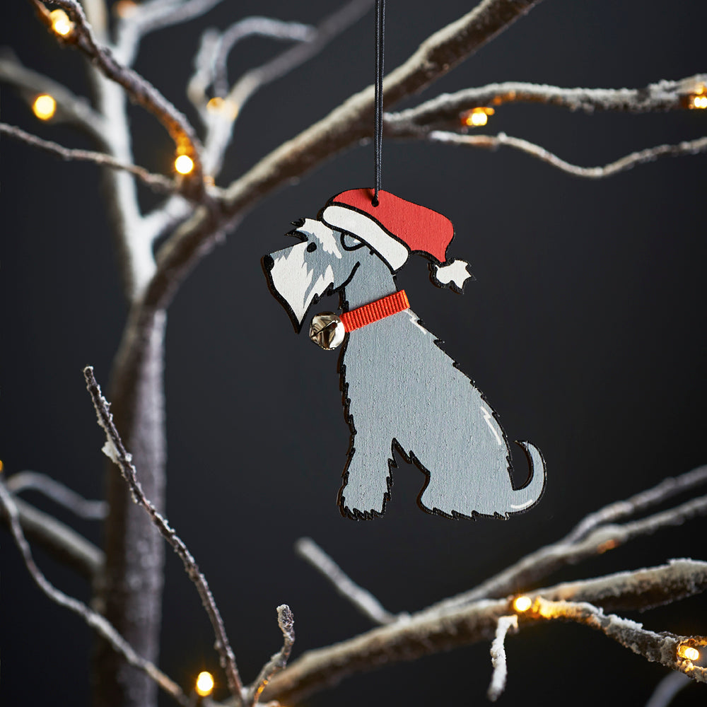 Grey Schnauzer Christmas tree decoration hanging on lit winter tree — wooden dog decoration with Father Christmas hat and jingle bell collar by Sweet William Designs