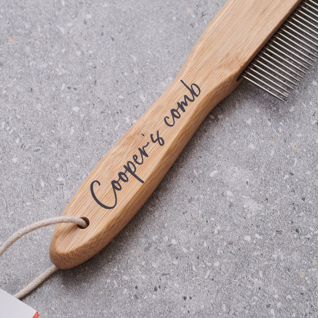 Close-up of personalised bamboo dog comb handle engraved with 'Cooper's comb' in script — metal-tooth grooming comb, dog lover gift by Sweet William Designs