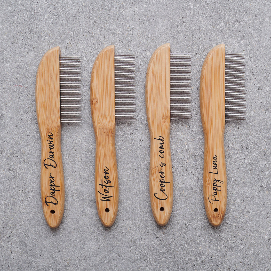 Four personalised bamboo dog combs with metal teeth laid in a row, engraved with dog names — Dapper Darwin, Watson, Cooper's comb and Puppy Luna — by Sweet William Designs