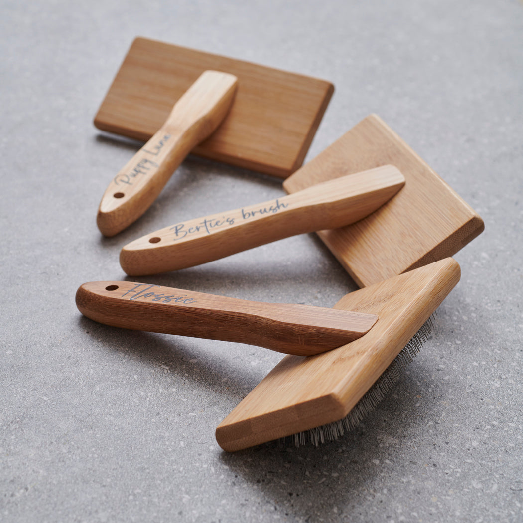 Three bamboo slicker brushes fanned out on grey stone — personalised with names, dog grooming gift by Sweet William Designs