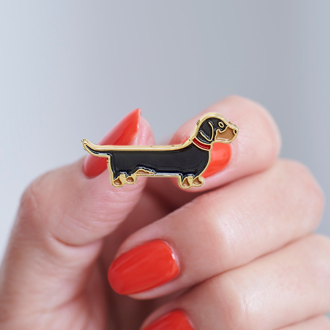 Close-up of a Dachshund enamel pin held in hand, showing the detailed Dachshund dog design by Sweet William Designs