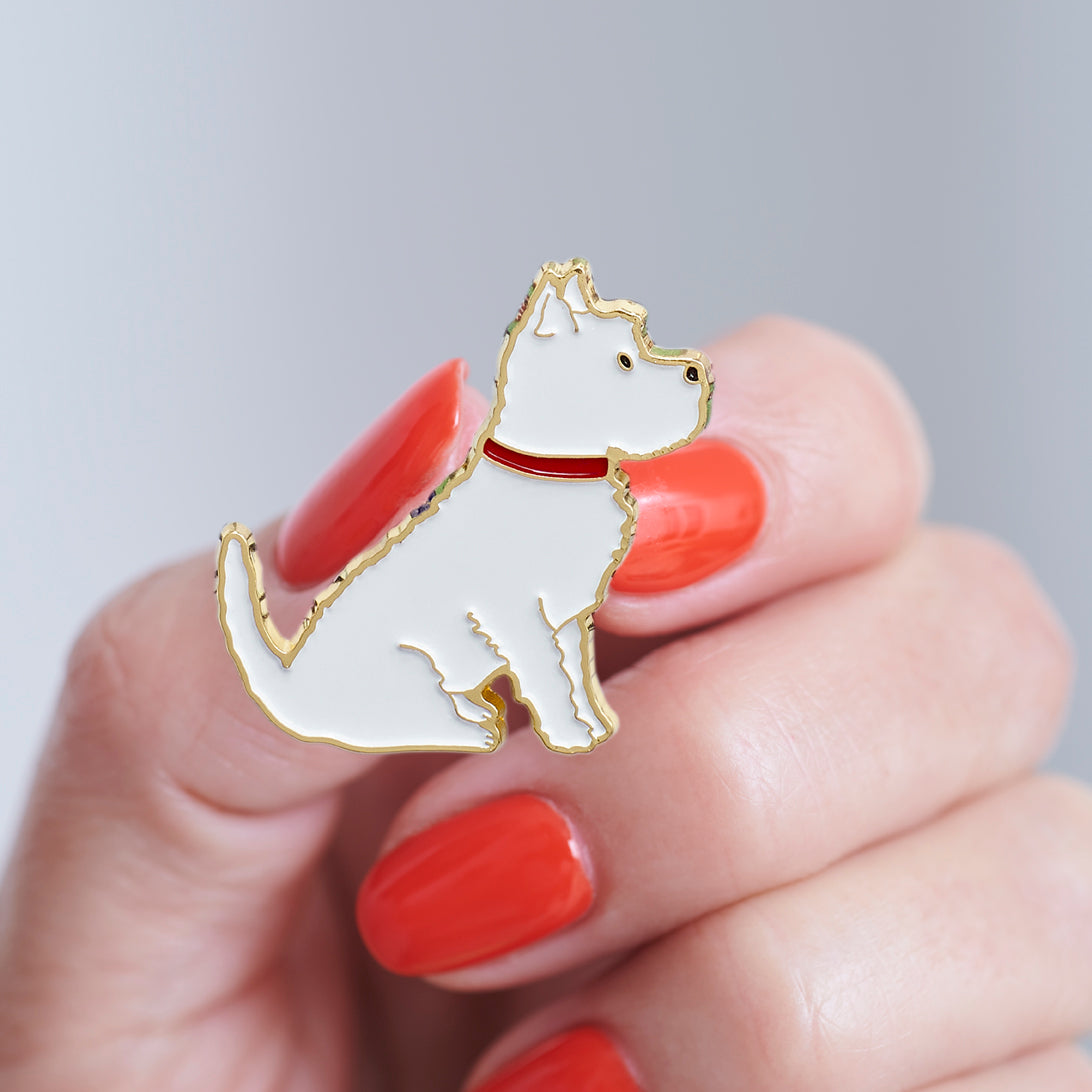Close-up of a Westie enamel pin held in hand, showing the detailed Westie illustration by Sweet William Designs