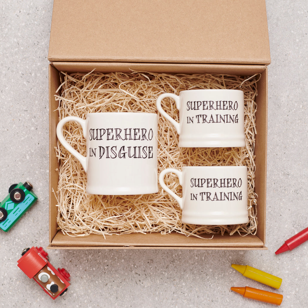 A perfect superhero gift set with one “Superhero in Disguise” mug and two “Superhero in Training” mugs, nestled in an open kraft gift box with shredded paper