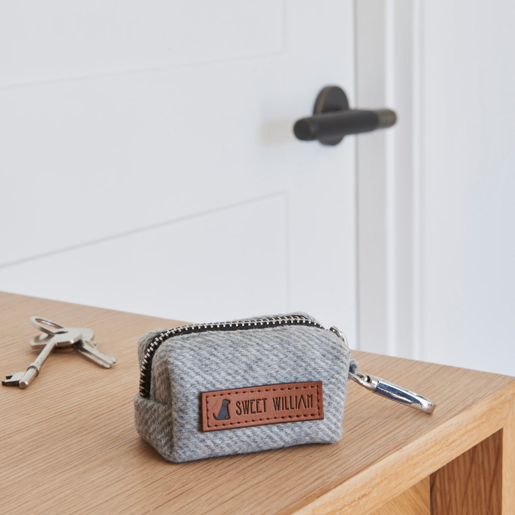 Close-up of the grey tweed poo bag holder on a wooden table, showing its woven fabric, zip and Sweet William label