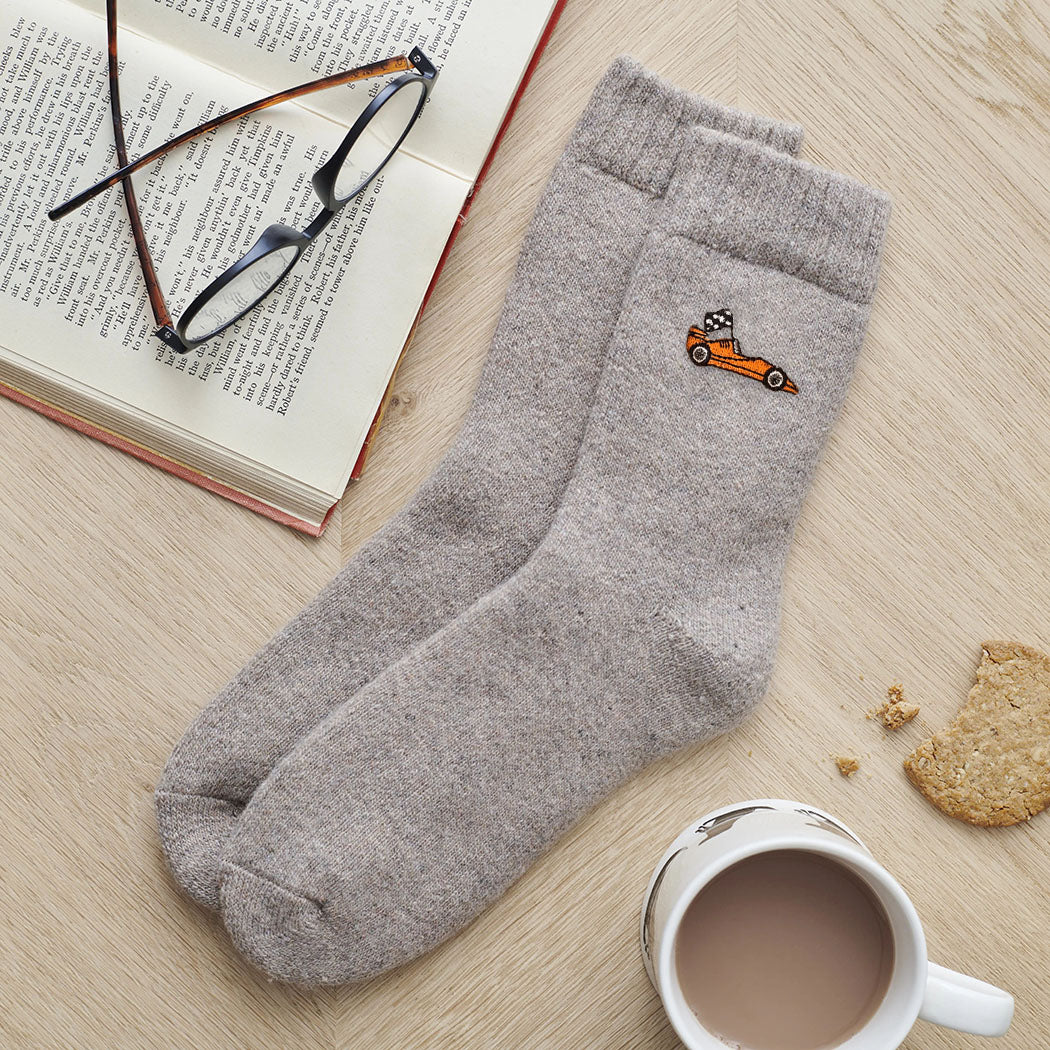 Orange racing car wool socks laid flat with book, glasses and cup of tea — a stylish gift for car enthusiasts by Sweet William Designs