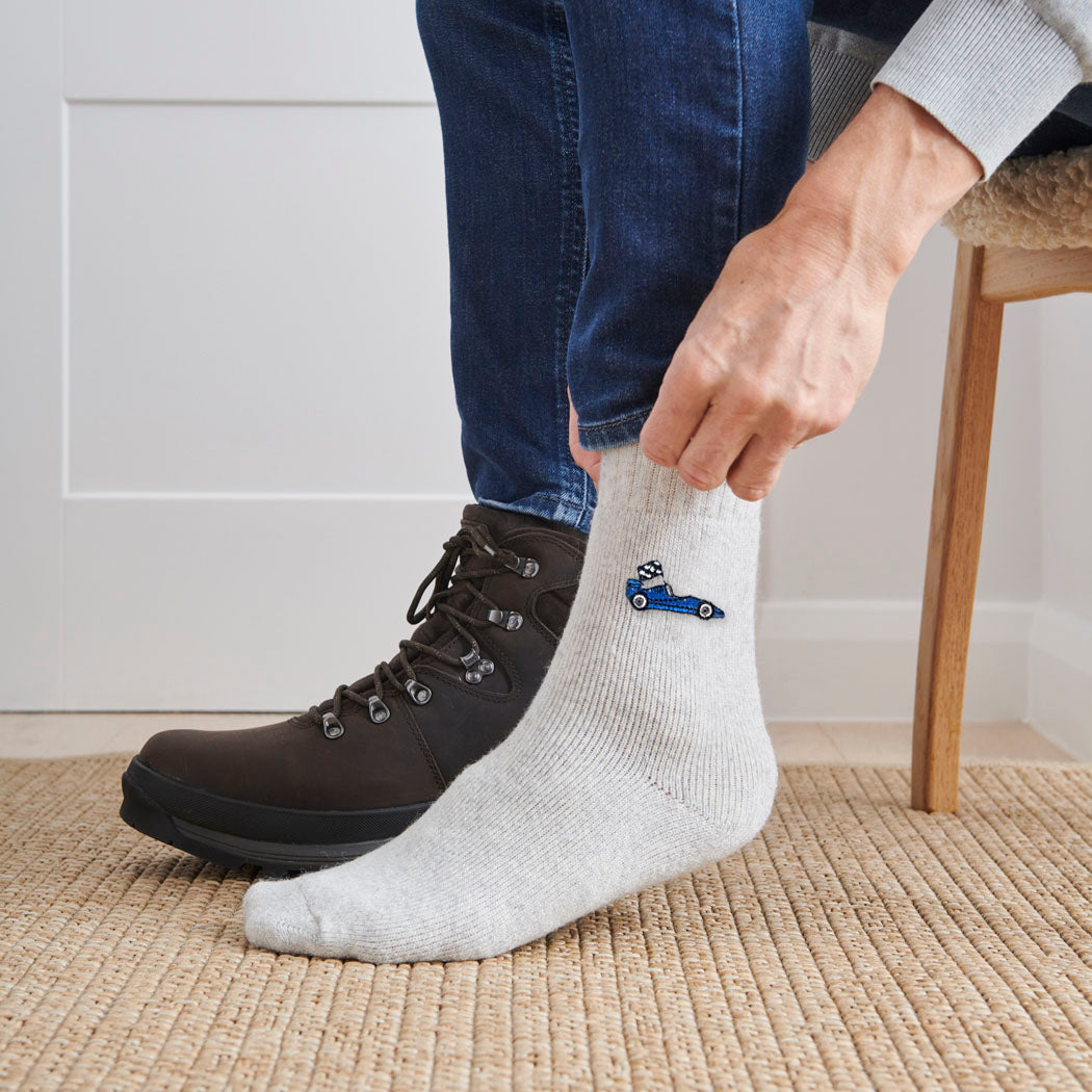 Man pulling on embroidered blue racing car wool socks with walking boots indoors — unisex motorsport-inspired wool blend socks by Sweet William Designs
