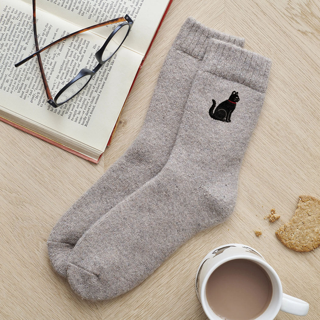 Black cat embroidered wool socks laid flat with book, glasses and cup of tea — cosy cat lover gift by Sweet William Designs