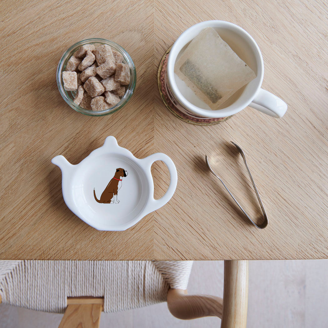 White teapot-shaped Boxer teabag dish with a brown and white dog illustration and red collar, beside a mug, sugar cubes and sugar tongs