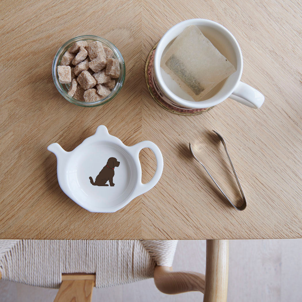 White teapot-shaped Chocolate Cockapoo / Labradoodle teabag dish with a brown dog illustration and red collar, beside a mug, sugar cubes and sugar tongs