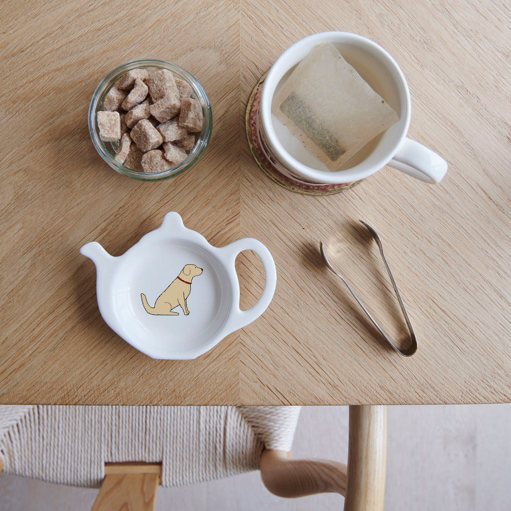 White teapot-shaped Golden Retriever teabag dish with a golden dog illustration and red collar, beside a mug, sugar cubes and sugar tongs