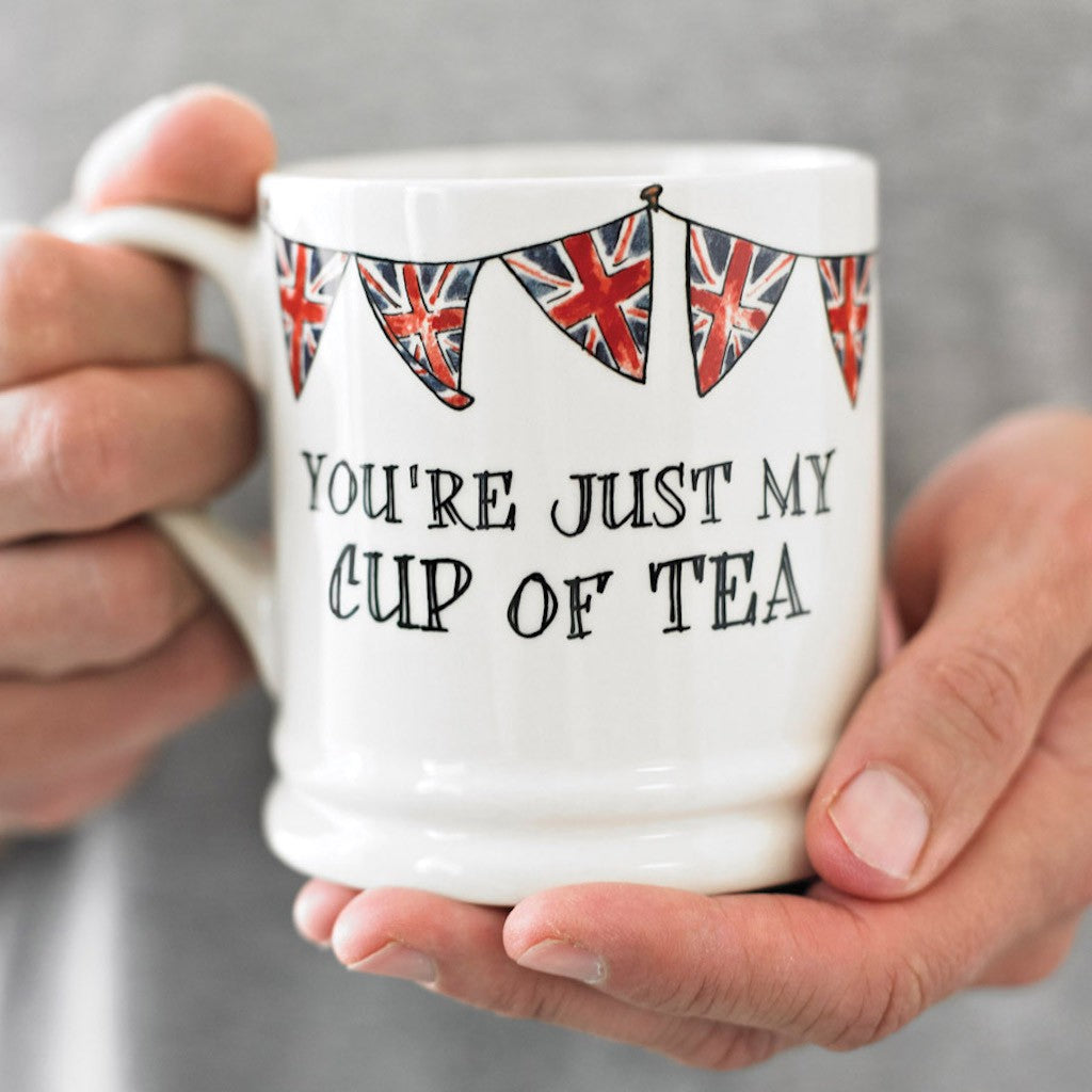 Porcelain mug held in both hands with Union Jack bunting and a “You’re just my cup of tea” message by Sweet William Designs