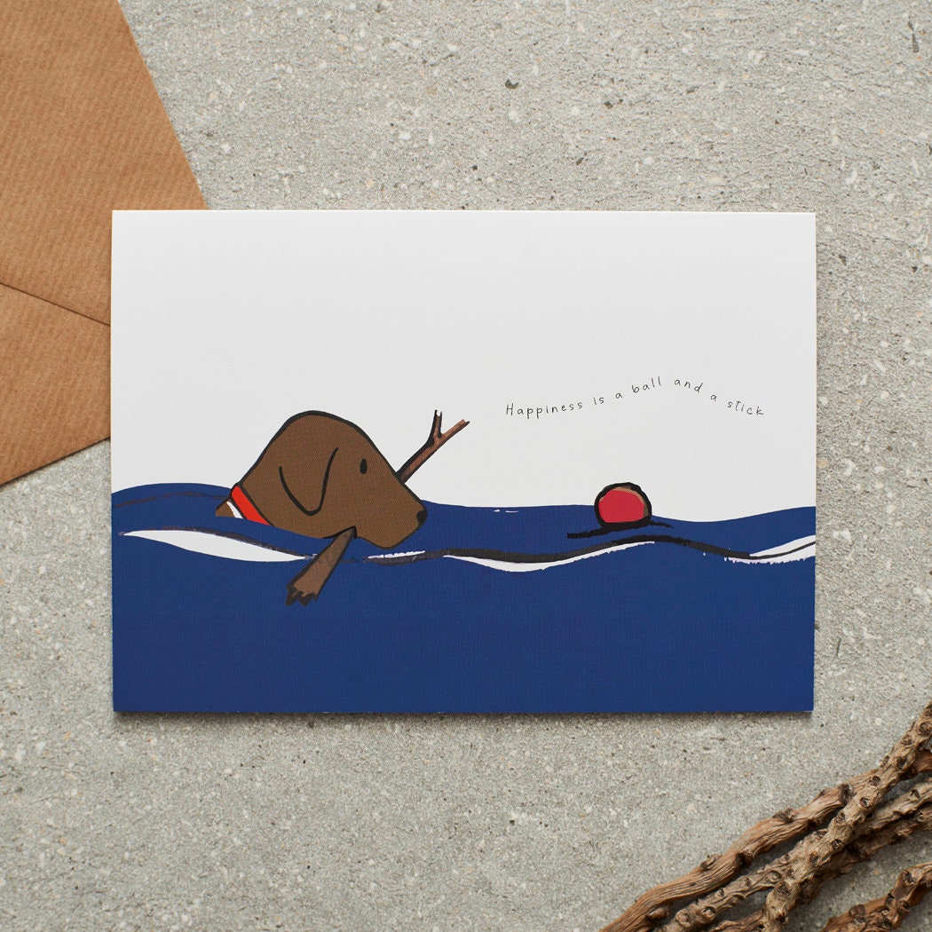 Swimming Chocolate Labrador card featuring a water-loving Chocolate Lab chasing a ball while holding a stick, with the words “Happiness is a ball and a stick” by Sweet William Designs