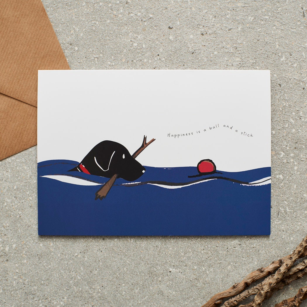 Swimming Black Labrador card featuring a water-loving Lab chasing a ball while holding a stick, with the words “Happiness is a ball and a stick” by Sweet William Designs