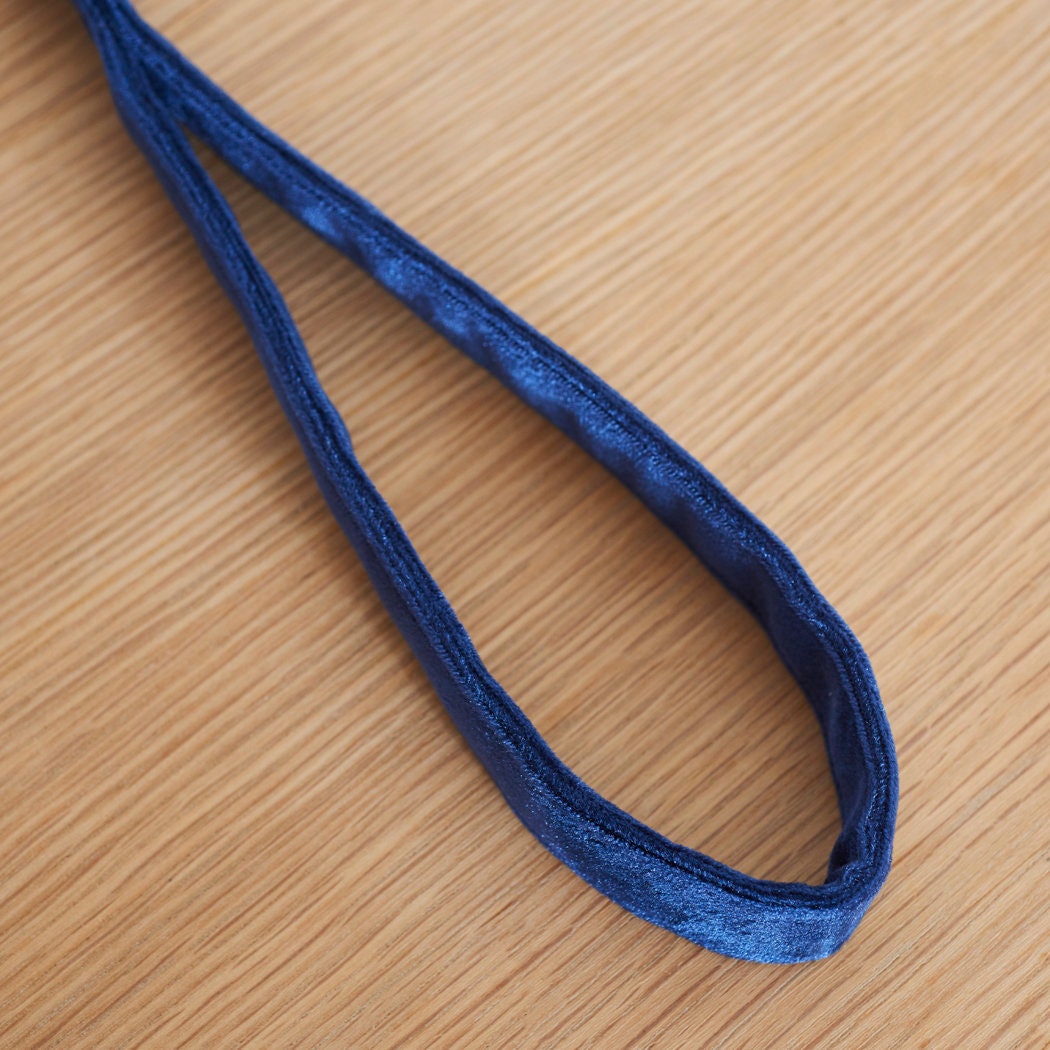 Soft navy velvet handle of the dog lead resting on a wooden table, with the fabric texture in focus