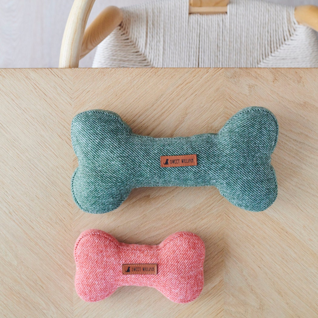 Green and orange tweed dog bone toys in two different sizes, displayed together on a wooden table