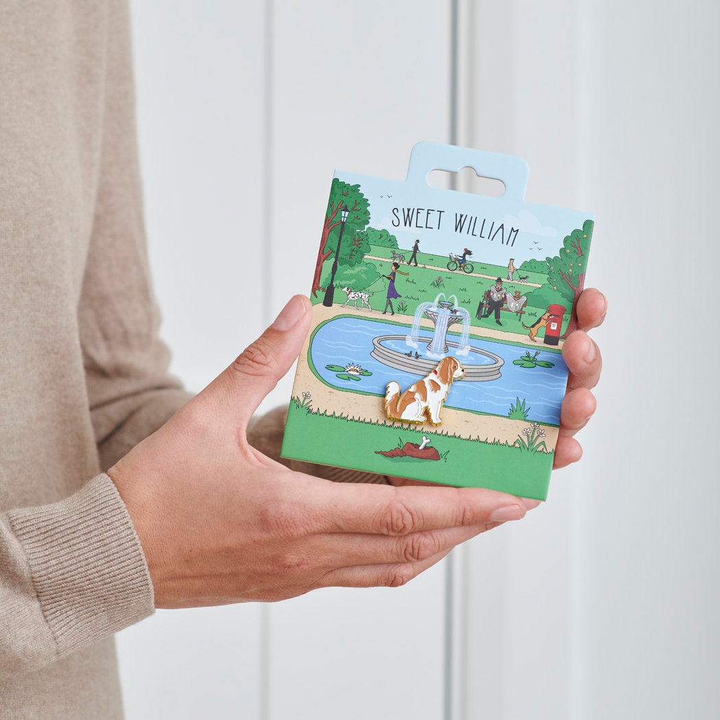 Cavalier King Charles Spaniel enamel dog pin held in hands on illustrated park backing card — gold-plated dog lover gift by Sweet William Designs