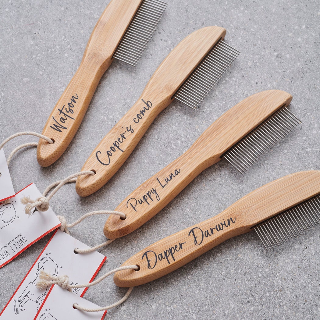Personalised bamboo dog combs with metal teeth and Sweet William branded tags, fanned out on grey stone