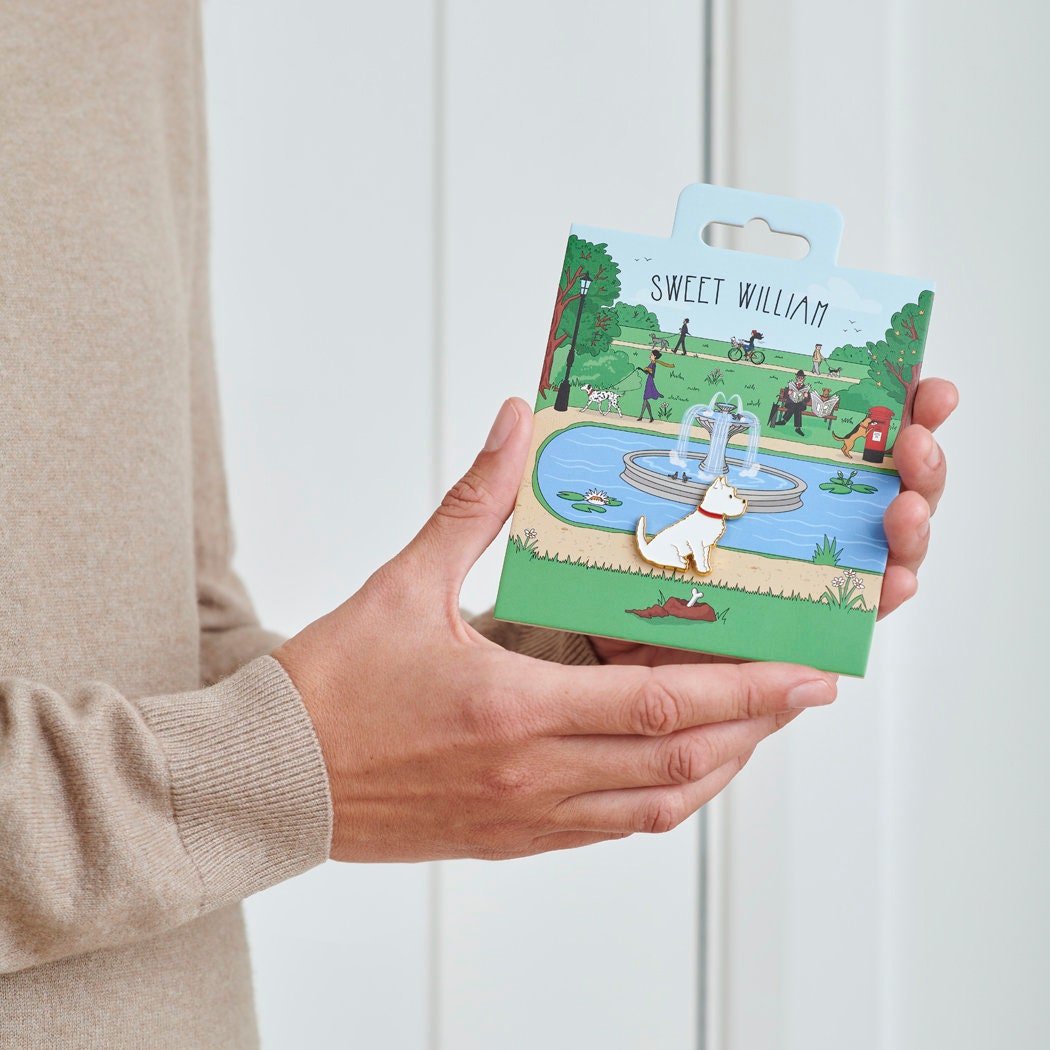 Westie enamel dog pin held in hands on illustrated park backing card — gold-plated dog lover gift by Sweet William Designs