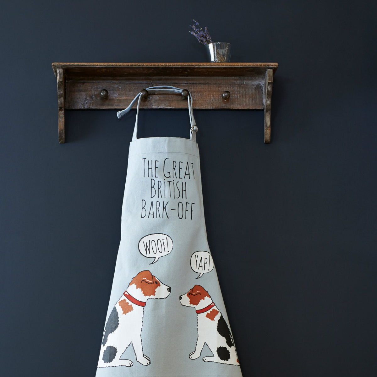 Jack Russell “The Great British Bark-Off” organic cotton apron hanging on wooden hooks, showcasing the full screen-printed design with two Jack Russell dogs, a fun gift for dog lovers