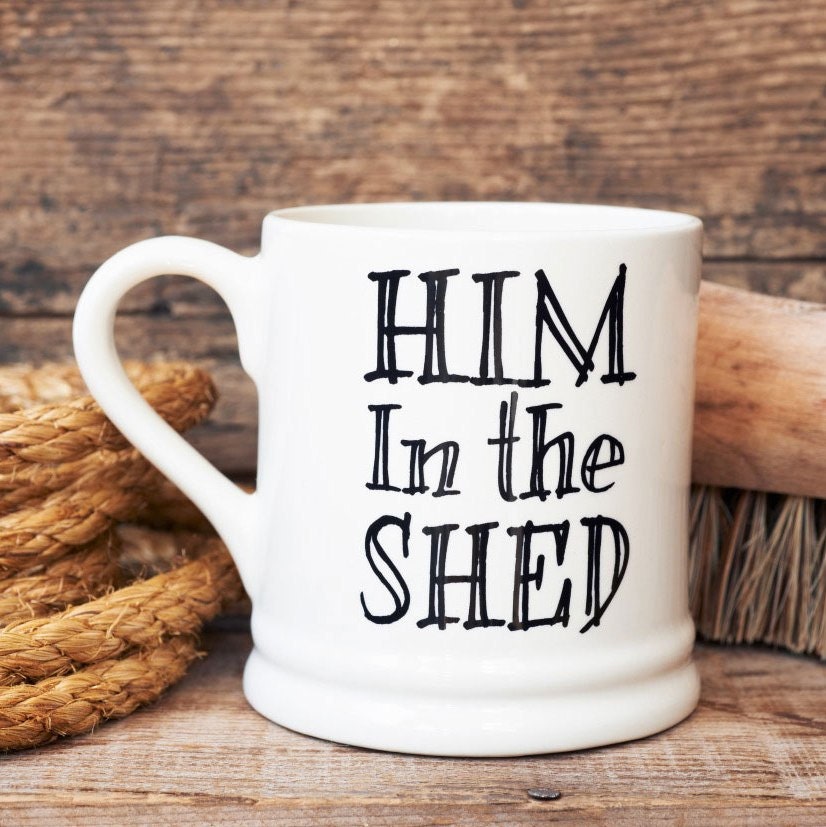 “Him in the Shed” ceramic mug, a funny gift for dads and grandads, styled with tools on a rustic wooden surface