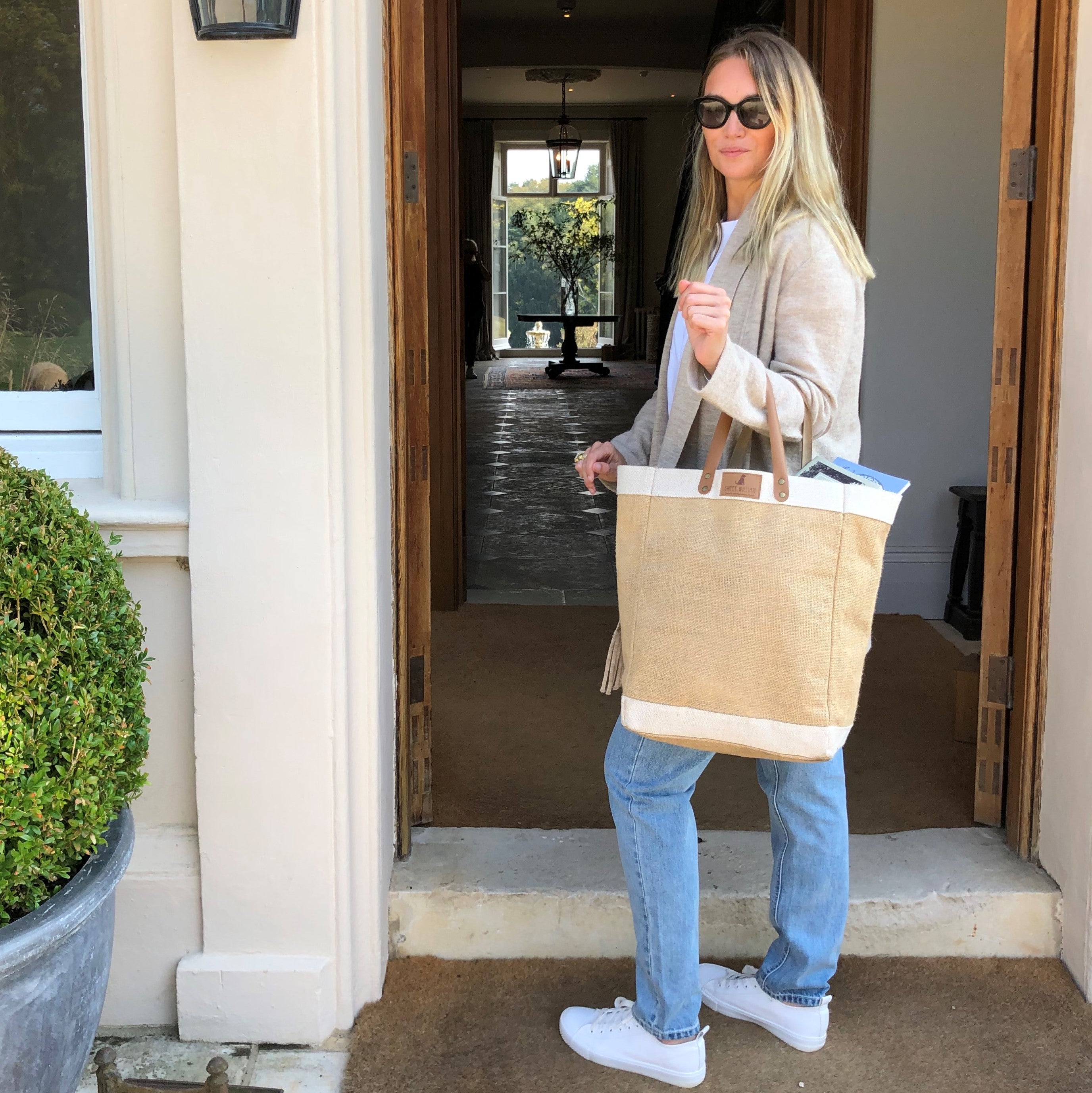 Woman carrying Sweet William jute bag at a front door — large natural jute tote with leather handles, ideal everyday bag