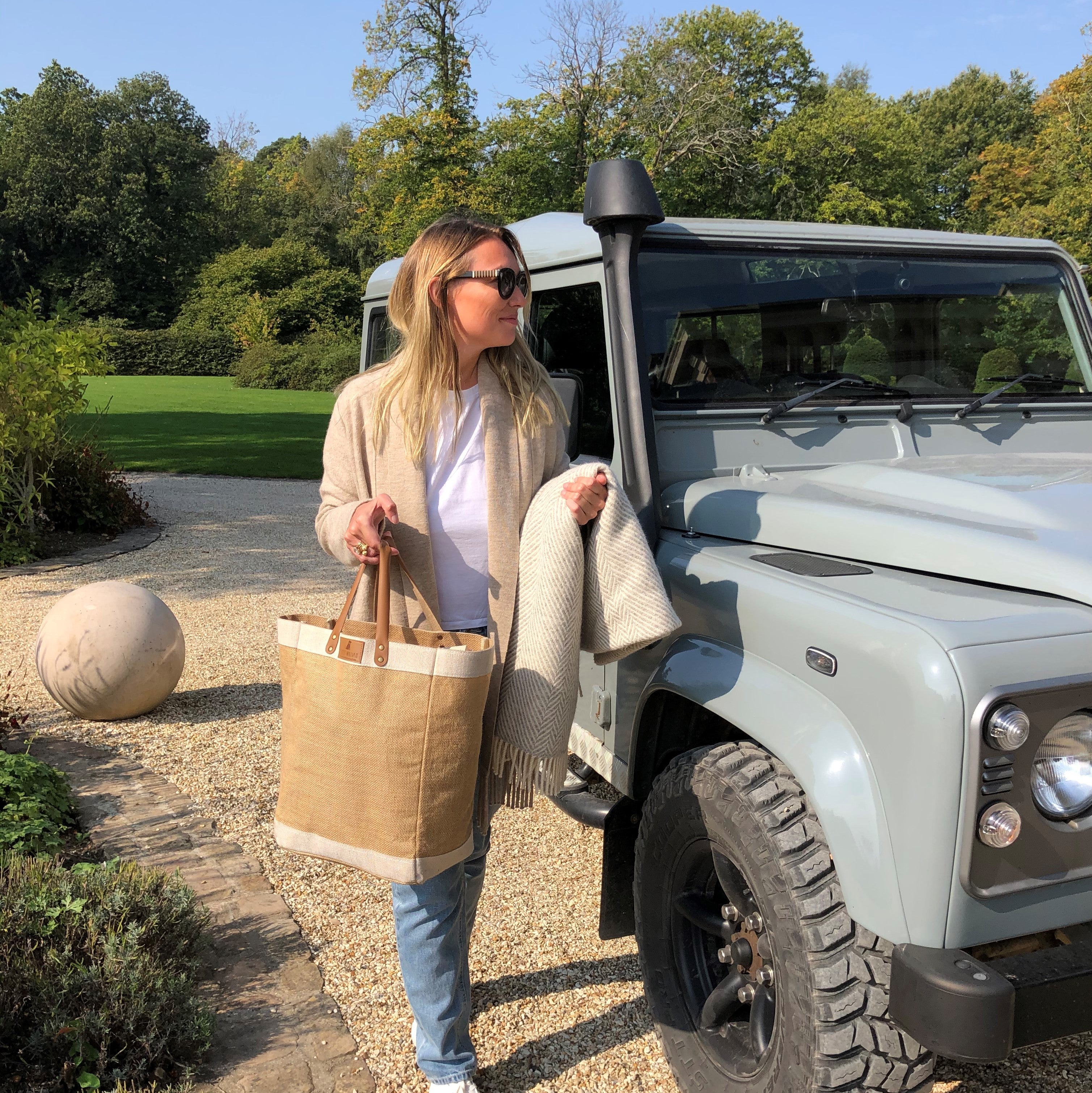 Woman carrying Sweet William jute tote bag beside a Land Rover — large jute bag with leather handles, perfect countryside companion