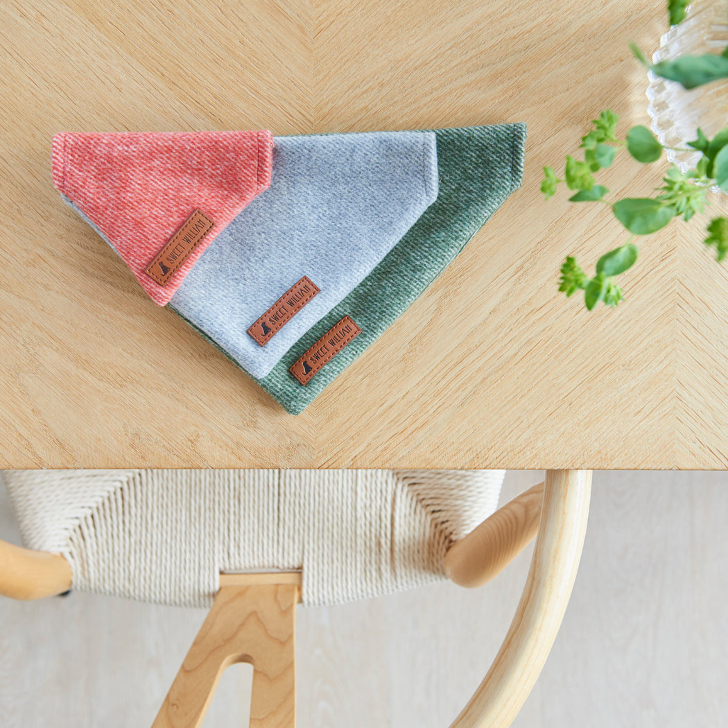 Orange, grey and green tweed dog bandanas with Sweet William labels, arranged together on a wooden table