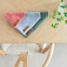 Orange, grey and green tweed dog bandanas with Sweet William labels, arranged together on a wooden table