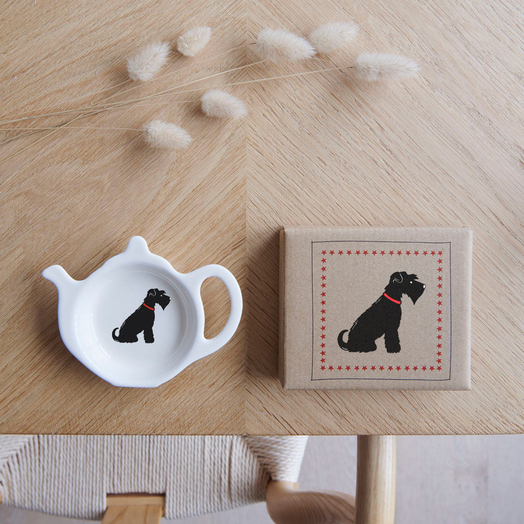 White teapot-shaped Black Schnauzer teabag dish beside its kraft gift box, both featuring a black Schnauzer illustration with a red collar