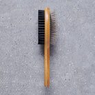 Bamboo double sided dog brush on grey stone surface showing both sides — bristle side and pin side, dog grooming brush by Sweet William Designs