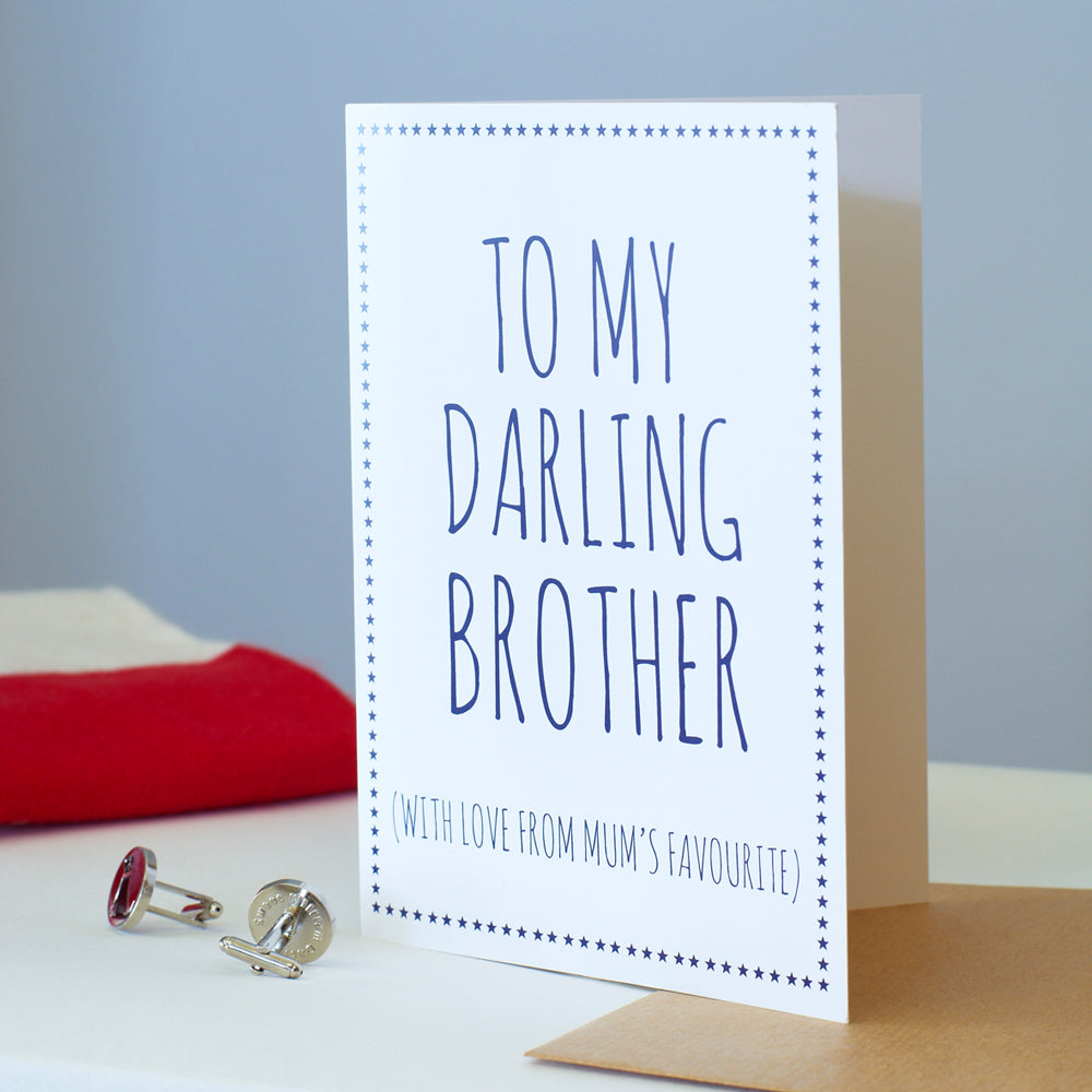 White Brother card with blue lettering reading “To My Darling Brother” and “With love from Mum’s favourite”, a blue star border, kraft envelope and silver cufflinks beside it.