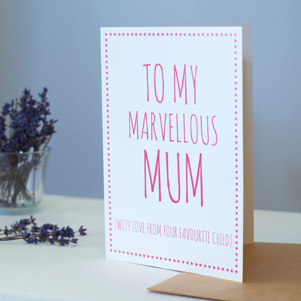 White Mum card with pink lettering reading “To My Marvellous Mum” and “With love from your favourite child”, a pink star border, kraft envelope and dried flowers.