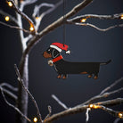 Dachshund Christmas tree decoration hanging on lit winter tree — wooden dog decoration with Father Christmas hat and jingle bell collar by Sweet William Designs
