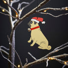 Pug Christmas tree decoration hanging on lit winter tree — wooden dog decoration with Father Christmas hat and jingle bell collar by Sweet William Designs