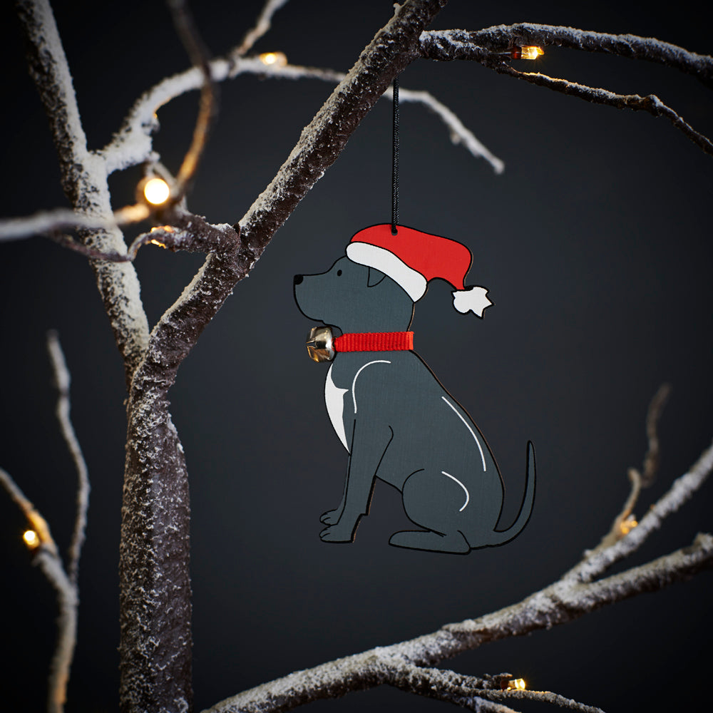Staffie Christmas tree decoration hanging on lit winter tree — wooden dog decoration with Father Christmas hat and jingle bell collar by Sweet William Designs