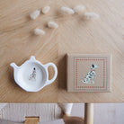 White teapot-shaped Dalmatian teabag dish beside its kraft gift box, both featuring a black-spotted Dalmatian illustration with a red collar