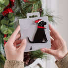 Black Labrador Christmas tree decoration held in hands on backing card — Father Christmas hat and jingle bell collar, dog lover gift by Sweet William Designs