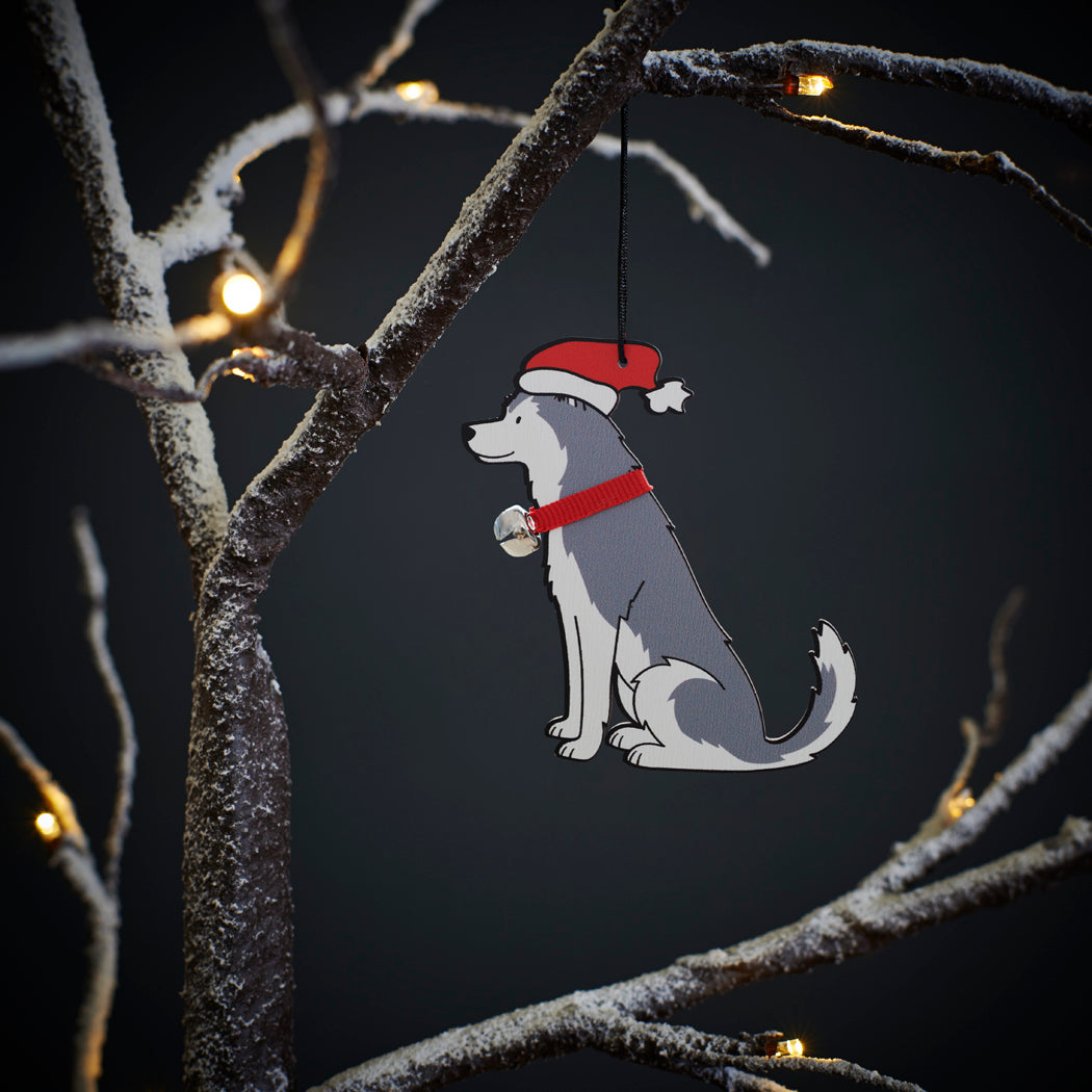 Husky Christmas tree decoration hanging on lit winter tree — wooden dog decoration with Father Christmas hat and jingle bell collar by Sweet William Designs