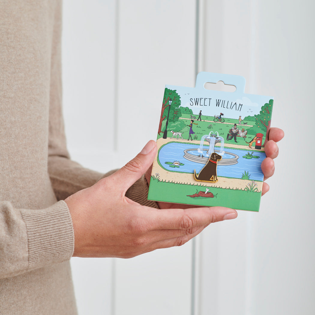Black Labrador enamel dog pin held in hands on illustrated park backing card — gold-plated dog lover gift by Sweet William Designs