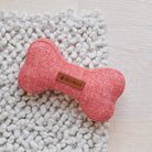 Orange tweed dog bone toy resting on a chunky white rug, showing its woven fabric and Sweet William label