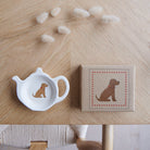 White teapot-shaped Golden Cocker Spaniel teabag dish beside its kraft gift box, both featuring a golden Spaniel illustration with a red collar