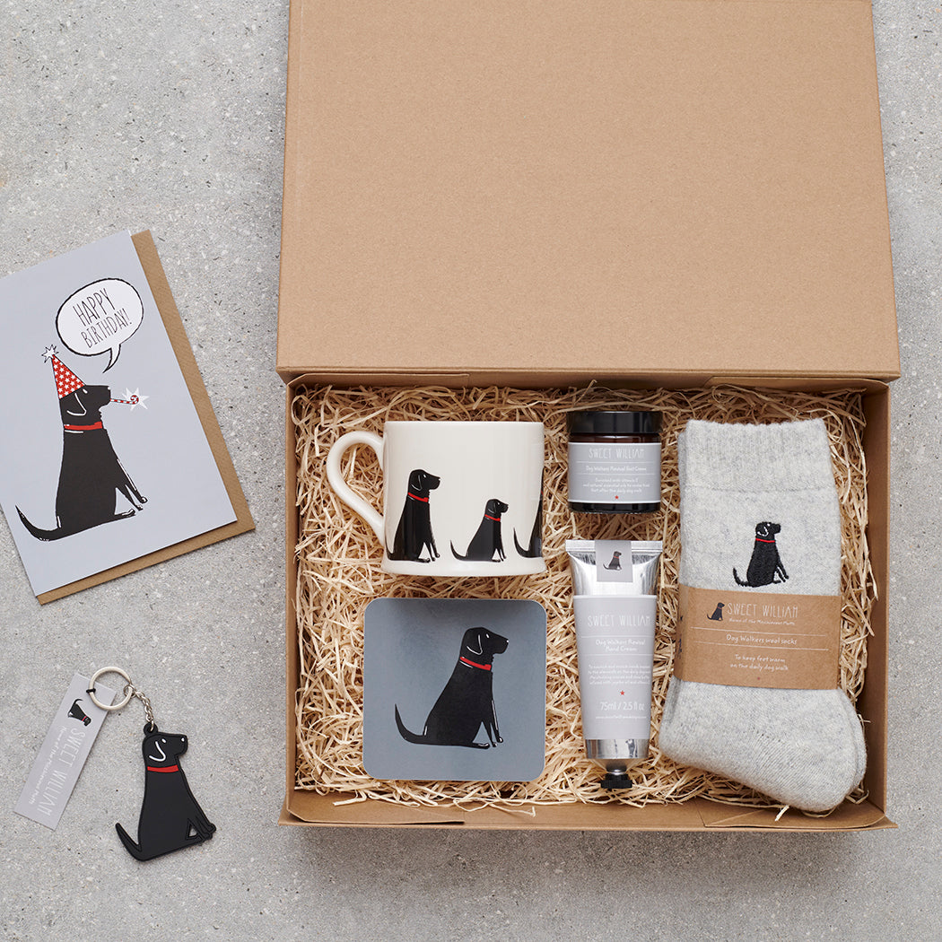 Black Labrador gift hamper featuring coaster, matching mug, socks, handcream and foot cream, beside a birthday card and keyring