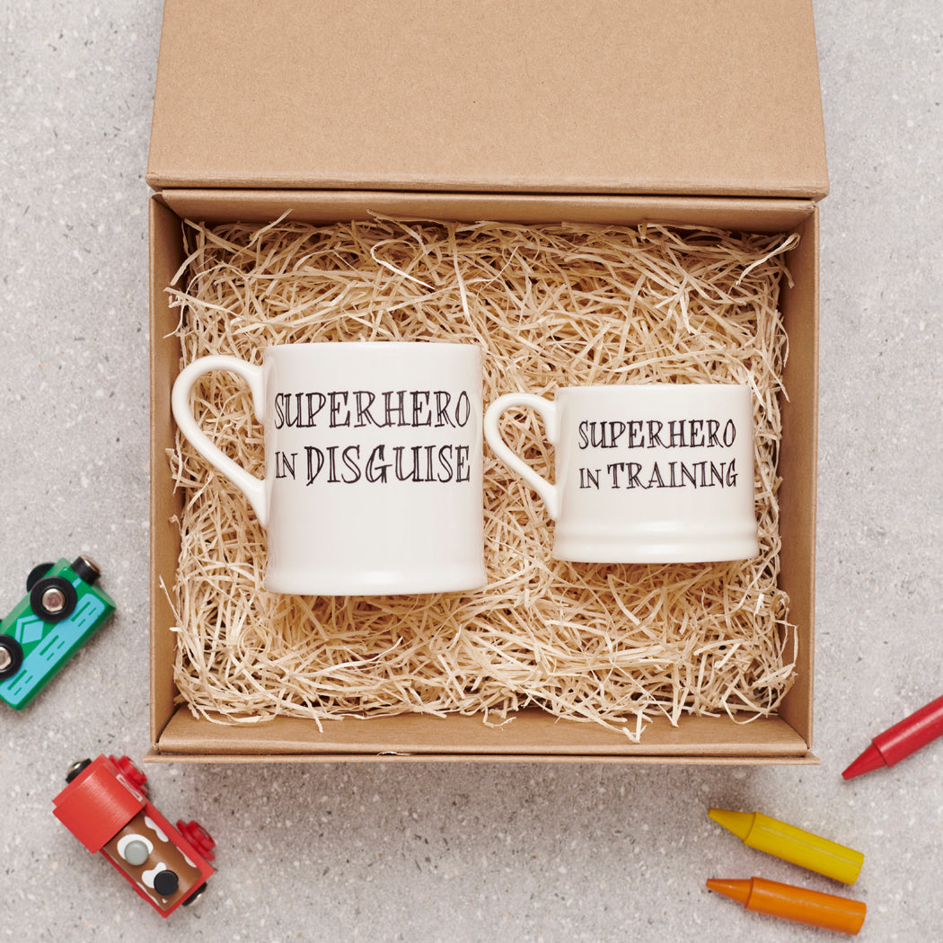 A perfect superhero gift set with “Superhero in Disguise” and “Superhero in Training” mugs nestled in an open kraft gift box by Sweet William Designs